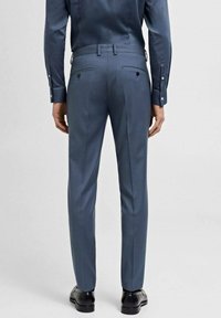 Modre hlače elegantnega kroja, slim-fit oblika, gladka tekstura, dve zadnji žepek s gumbi, oblečene z ujemajočo se srajco in črnimi čevlji.
