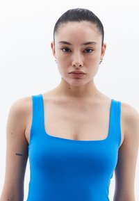 Top azul sin mangas con escote cuadrado, hecho de un material suave, que presenta una silueta ajustada. Sencillo, de un color sólido sin patrones.