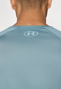 Camiseta atlética azul hecha de una tela suave y ligera, con un diseño de manga raglán y un logotipo sutil en la nuca de la espalda.