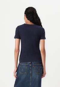 Navyblå kortærmet t-shirt med ribbet tekstur og rund halsudskæring, båret med en denimnederdel med stiksyninger og lommer.
