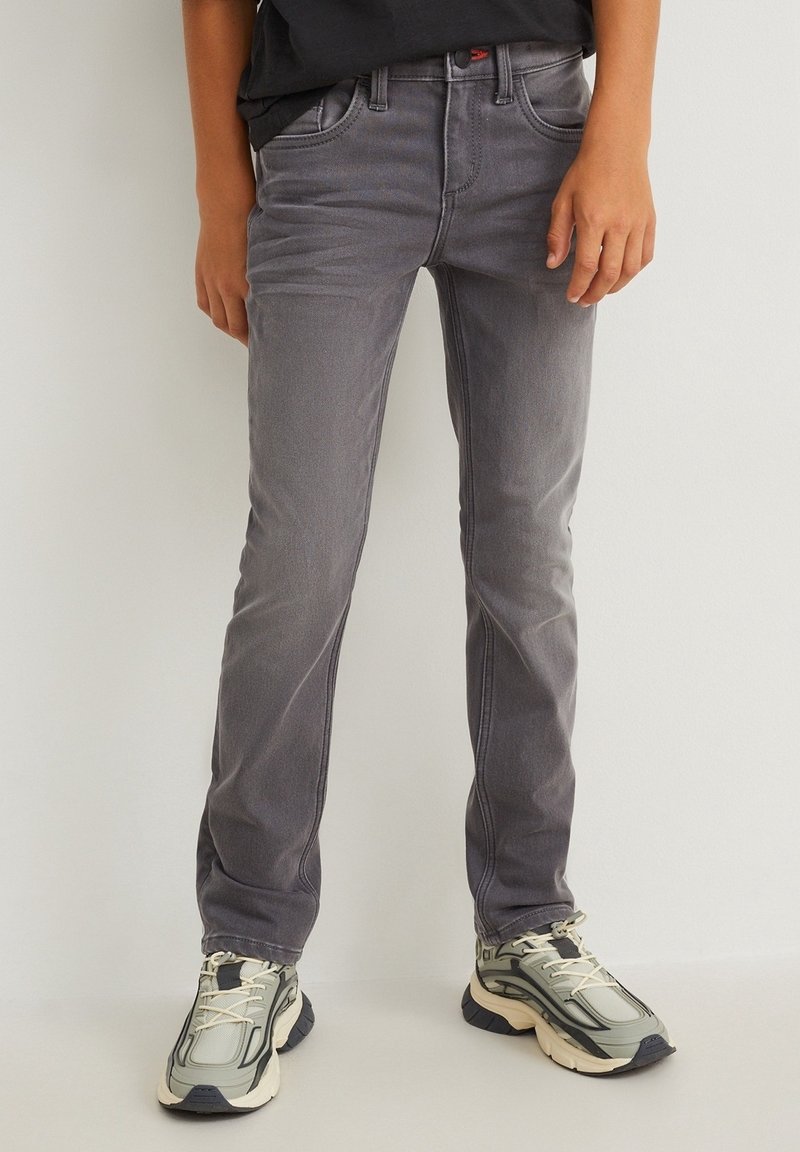 Jean gris slim avec cinq poches, texture délavée et coutures contrastantes, associé à des baskets volumineuses gris clair.