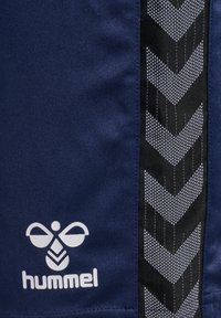 Ciemnoniebieska tkanina z czarno-białym paskiem w jodełkę i białym logo Hummel z stylizowaną pszczółką oraz tekstem.