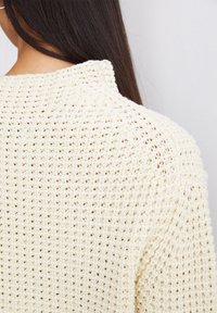 Cremfarbener Strickpullover mit offener Maschenstruktur. Verfügt über einen runden Halsausschnitt und leicht versetzte Schulternähte. Die Rückansicht zeigt das Hauptmuster.