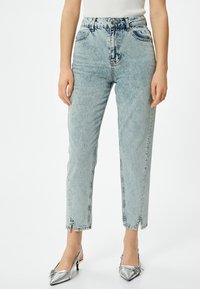 Ljust tvättade jeans med hög midja, rak benform och framtida slitsar vid vristen; kombinerat med metalliska silverfärgade slingbacks.