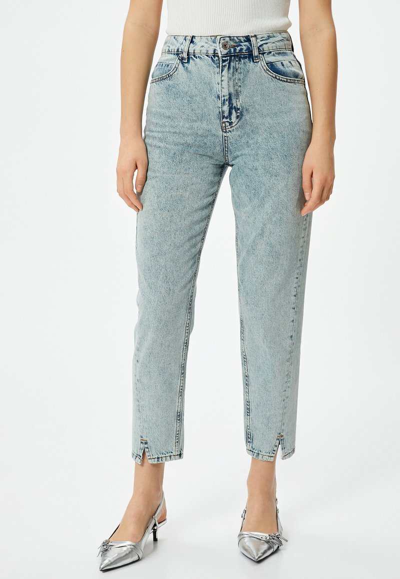 Ljust tvättade jeans med hög midja, rak benform och framtida slitsar vid vristen; kombinerat med metalliska silverfärgade slingbacks.