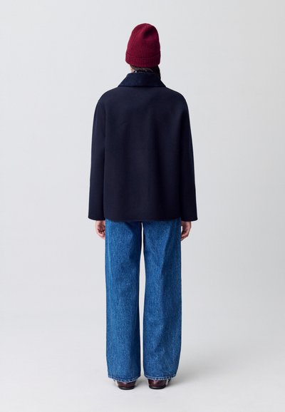 Cappotto di lana navy con collo ampio, abbinato a jeans di denim blu larghi e un berretto di maglia ribattuto bordeaux.