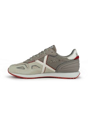 Zapatilla deportiva en gris y crema, con material de ante y malla, detalles en rojo, patrones texturizados y suela de goma. Se muestra en vista lateral.