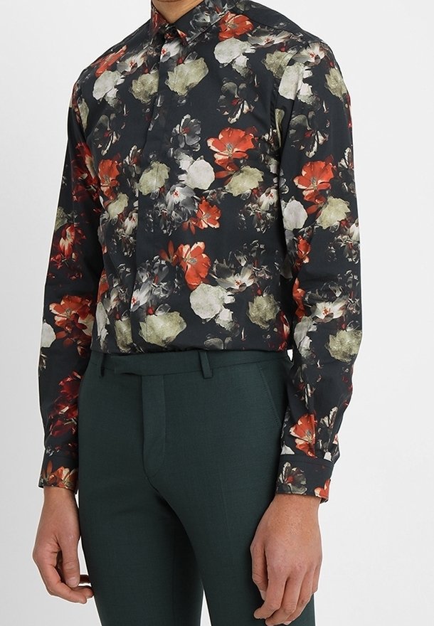 Chemise noire à manches longues avec des motifs floraux rouges, beiges et gris, associée à un pantalon sur mesure vert foncé.