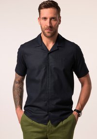Camisa de botón de manga corta en un tejido texturizado de un color azul marino oscuro. Presenta un collar tipo extendido y un sutil logo bordado en el pecho.