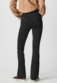 Vaqueros negros de campana, hechos de mezclilla, con una cintura de tiro medio. Presentan dos bolsillos traseros y detalles de costura sutiles. Combinados con zapatillas negras.