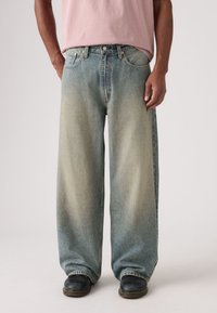 Svetlomodré džínsové nohavice s voľným strihom, výrazným vyblednutým efektom, piatimi vreckami a medenými nitmi. Lem je voľný a rovný.