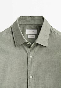 Chemise homme vert clair boutonnée avec col pointu et étiquette de marque visible à l'intérieur du col.