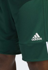 Grüne Sportshorts aus atmungsaktivem Material, mit weißem Adidas-Logo und seitlichen Streifen, texturiertem Oberflächenstruktur und elastischem Bund.