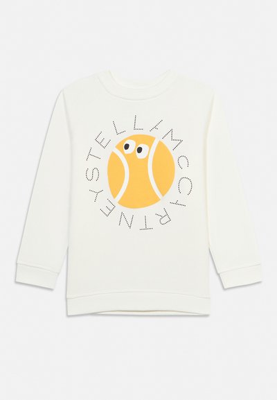 Balta garroku krekls ar dzeltenas tenisbola grafiku, kurā ir acis un teksts "Stella McCartney" ap to aplīša rakstā.