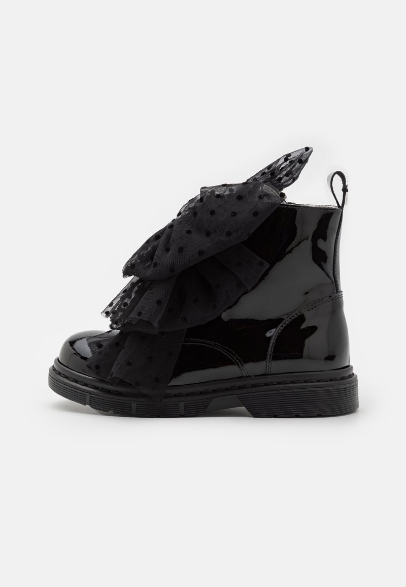 Bottine en cuir verni noir avec des volants en tulle noir à pois superposés sur le devant et une bride d’extraction au talon.