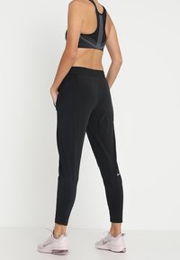 Černé sportovní kalhoty se zúženým střihem a elastickým pasem, s bočními panely a malým bílým logem Nike na kotníku.