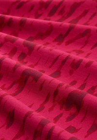 Roter Stoff mit einer weichen Textur, der ein Farbverlaufsmuster aus dunkleren roten Streifen aufweist, was visuelle Tiefe und Bewegung erzeugt.