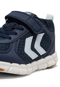 Marineblauwe sportschoen met een gestructureerde bovenkant, mesh panelen en lichtblauwe accenten. Voorzien van een klittenbandsluiting en een rubberen zool met ribbels.