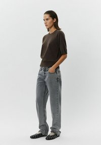 Brown short-sleeve knit sweater, gray high-waisted jeans, and black studded slip-on shoes; model stands in a neutral background.