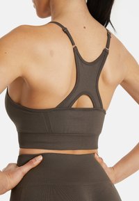 Sportivo color marrone con design a racerback, realizzato in materiale liscio. Presenta spalline regolabili e dettagli a taglio sul retro.