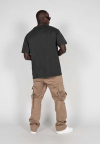 Mørkegrå kortermet t-skjorte kombinert med beige cargo-bukser med sidelommer, iført hvite joggesko. Bakgrunnen er ensfarget hvit.