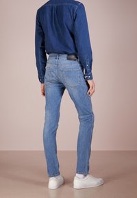 Blå denimjeans med slim fit, med medelhög midja, bakfickor och en mjuk textur, tillsammans med vita sneakers och en blå skjorta.