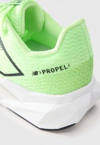 Zöld és fehér New Balance Propel futócipő sarok, textúrált mintázattal és fekete logóval, fehér háttér előtt.