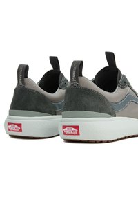 Grå och mörkgröna sneakers i mocka och nätmaterial, med en texturerad vit mellansula och en röd Vans-logotyp på hälen.