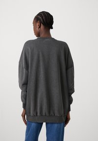 Oversized gray sweatshirt with ribbed crew neckline and cuffs, elastic hem, and soft texture, paired with blue denim jeans.