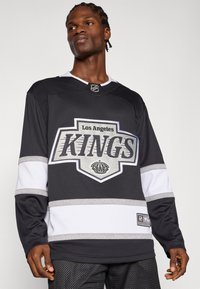 Must küllane Los Angeles Kings jäähoki särk valgete ja hõbedaste aktsentidega, mille esiküljel on meeskonna logo ja kroonembleem. Pika varrukaga disain.