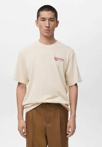 Beige cotton t-shirt with short sleeves, round neckline, and red "Equestrian Pride" graphic on the left chest. Flat, smooth texture.