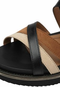 Sandale en cuir noir et suède beige avec des brides croisées. Semelle intérieure rembourrée et semelle en caoutchouc, avec un accent métallique le long du bord.