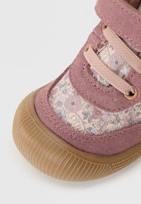 Buty na rzep w stonowanym różowym zamszu z kwiatowym wzorem na tkaninie. Okrągła gumowa podeszwa z teksturowanym gripem. Posiada elastyczne sznurowadła do regulacji dopasowania.