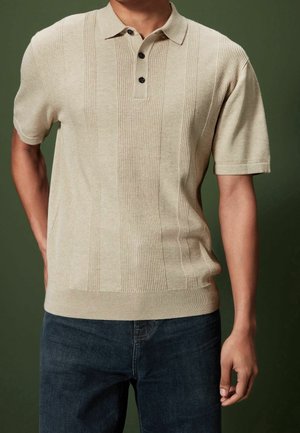 Beige neulepolo, jossa on pystysuorat ribbikuvioinnit, kolme mustaa nappia, lyhyet hihat ja slim-fit-muotoilu, yhdistettynä tummaan farkkuihin.