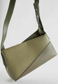 Grüne Leder-Umhängetasche mit geometrischem Design, glatter Textur, schräger Form und verstellbarem Tragegurt.