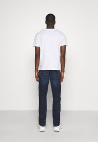 Hvit t-skjorte med kort erm parret med mørkeblå jeans. Jeansene har en klassisk fem-lommestil og subtil baklommesting.