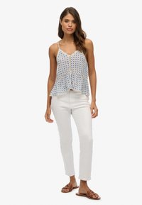 Mouwloze peplumtop met bloemenpatroon in lichtblauw met wit, voorzien van een v-hals en fijne kantafwerking, gecombineerd met witte skinny pants en bruine sandalen.