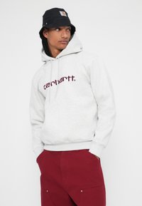 Sivá mikina s kapucňou a burgundským logom "carhartt.", s ovládaním šnúrkami a voľným strihom, kombinovaná s marónovými nohavicami.