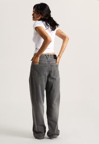 Grå denimjeans med en afslappet pasform, der har dobbelt baglomme, kontrastsying og en lav talje. Bruges sammen med en hvid tætsiddende top.