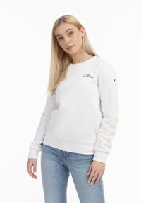 Felpa bianca realizzata in tessuto morbido, con scollatura rotonda, maniche lunghe e un piccolo logo nero sul petto. Jeans azzurri chiari.