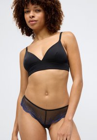Čierny trojuholníkový bralet s tenkými ramienkami, spárovaný s čiernymi spodnými nohavičkami z jemného sieťovaného materiálu s modrým čipkovým lemom pozdĺž okrajov.