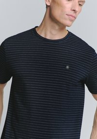 Marineblauwe t-shirt met korte mouwen, voorzien van dunne horizontale strepen, een geribbelde ronde hals en een klein hexagonaal logo op de borst.