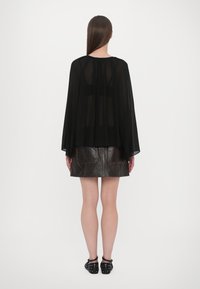 Sheer black blouse with flowing sleeves, layered over a dark leather skirt featuring patch pockets and contrasting stitching. Black footwear.
