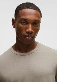 Világosszürke, kerek nyakú póló, rövid ujjú és sima textúrájú, egy rövid hajú, semleges arckifejezésű modell viseli.