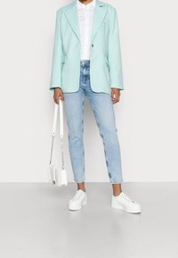 Světlomodré sako s širokými klopami, ve spojení s bílou košilí na knoflíky a světlomodrými džínami. Na nohou bílé tenisky na platformě, drží bílou tašku.