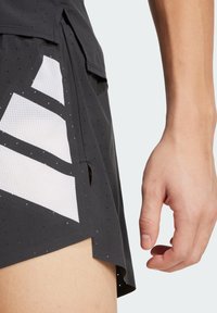 Shorts de sport noirs en tissu texturé, avec de grandes découpes géométriques blanches et des perforations pour la respirabilité.