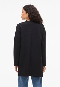 Μαύρο υφασμάτινο μακρύ παλτό με ίσια κοπή, χαμηλωμένους ώμους και μακριά μανίκια. Διαθέτει απλό ψηλό λαιμό και λεπτομέρεια ραφής στην πλάτη.