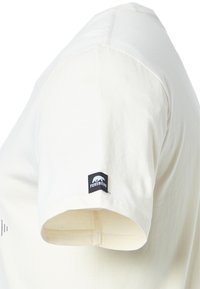 Camiseta de manga corta color crema hecha de algodón suave, con una pequeña etiqueta negra del logo de Forsberg en la manga y elementos de diseño minimalistas.