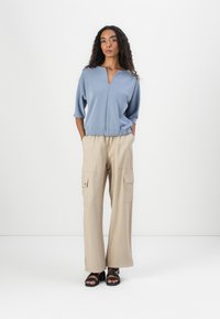 Top azul claro de manga curta com decote em V e cintura franzida, combinado com calças cargo largas beje com bolsos laterais.