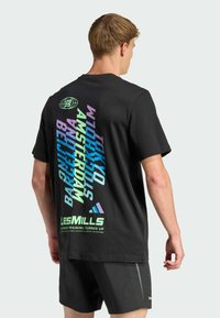 Camiseta de algodón negra con texto vibrante en diagonal en azul, púrpura y verde, que enumera ciudades y marcas. Mangas cortas, corte relajado.
